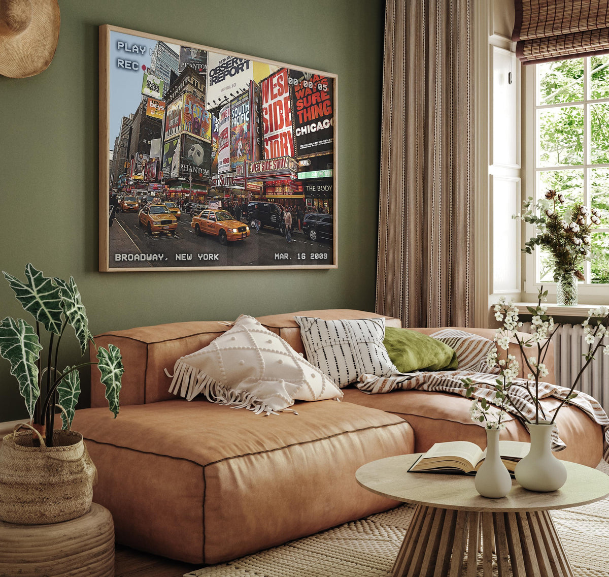Retro VHS Broadway poster in oak frame hung above a tan leather sofa on a green wall
