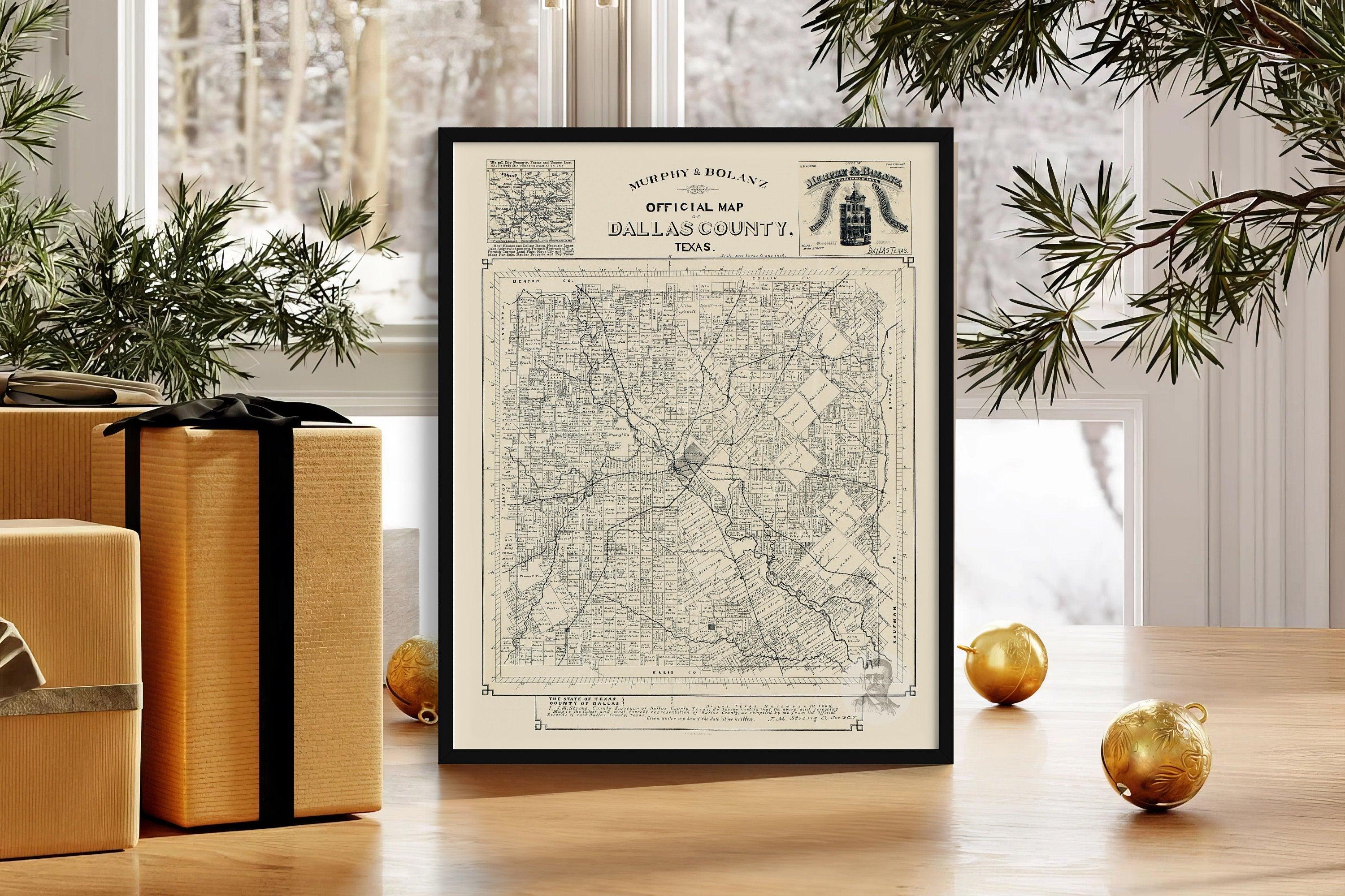 Framed antique Dallas County Texas map print resting on a table beside gold ornaments and wrapped gifts