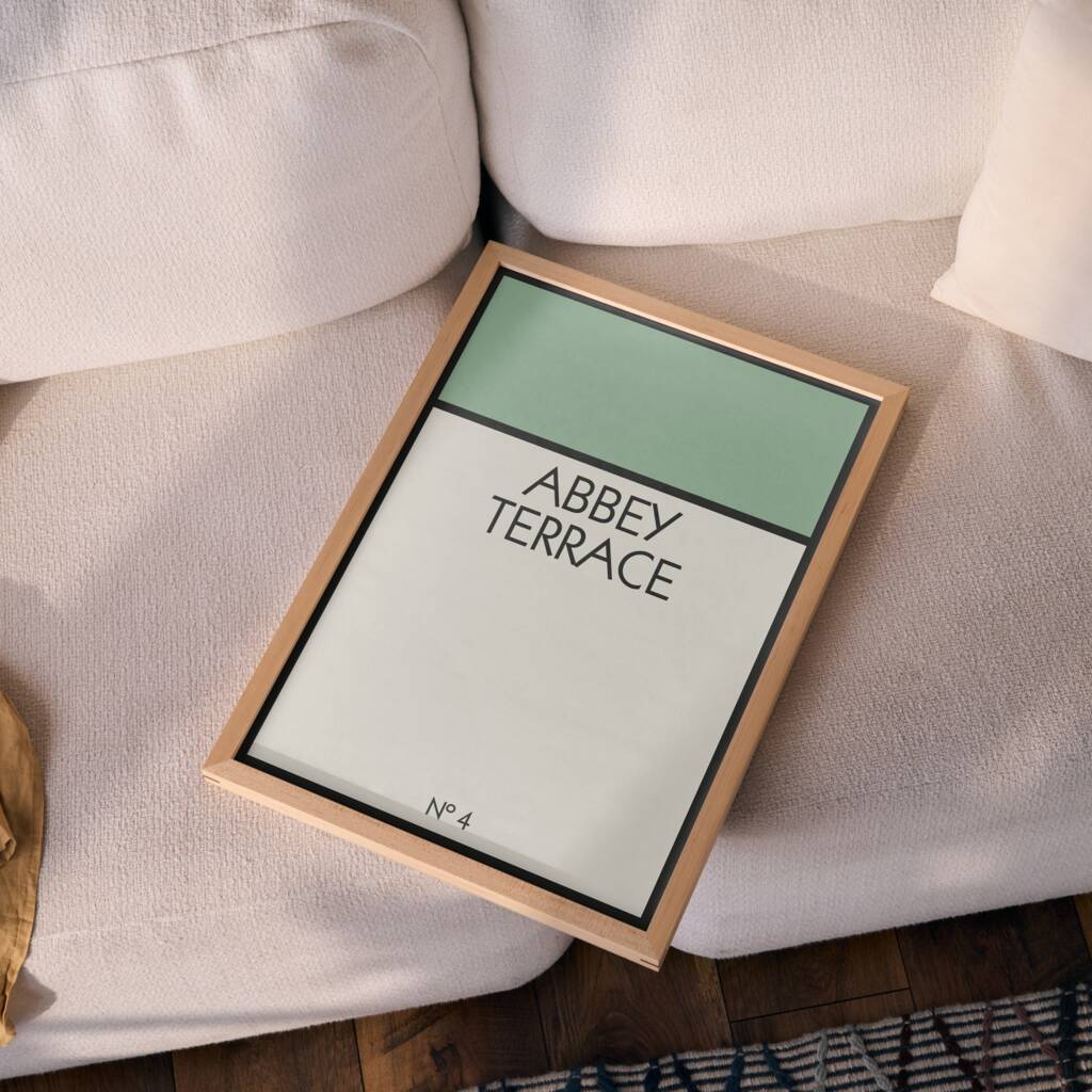 Framed board game style address print reading Abbey Terrace No 4 resting on cream sofa